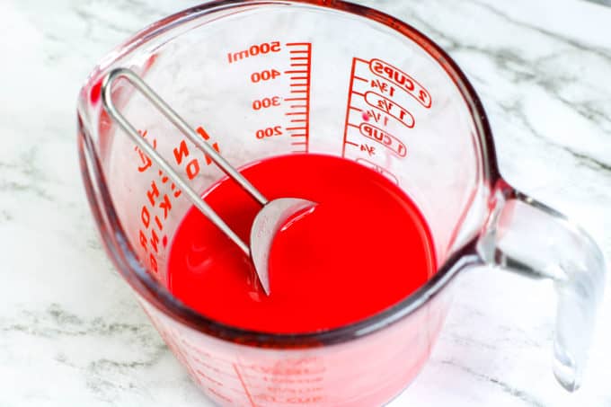 mixing red paint and water in glass measuring cup