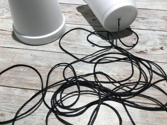 For each cup, poke a small hole, insert then end of the string and tie a knot.