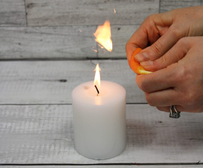 Student squeezing orange peel near candle during combustion science experiment
